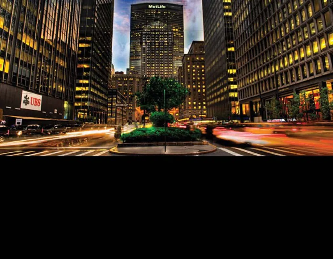 A city intersection at dusk, office towers lit from within, traffic drawn into long light trails